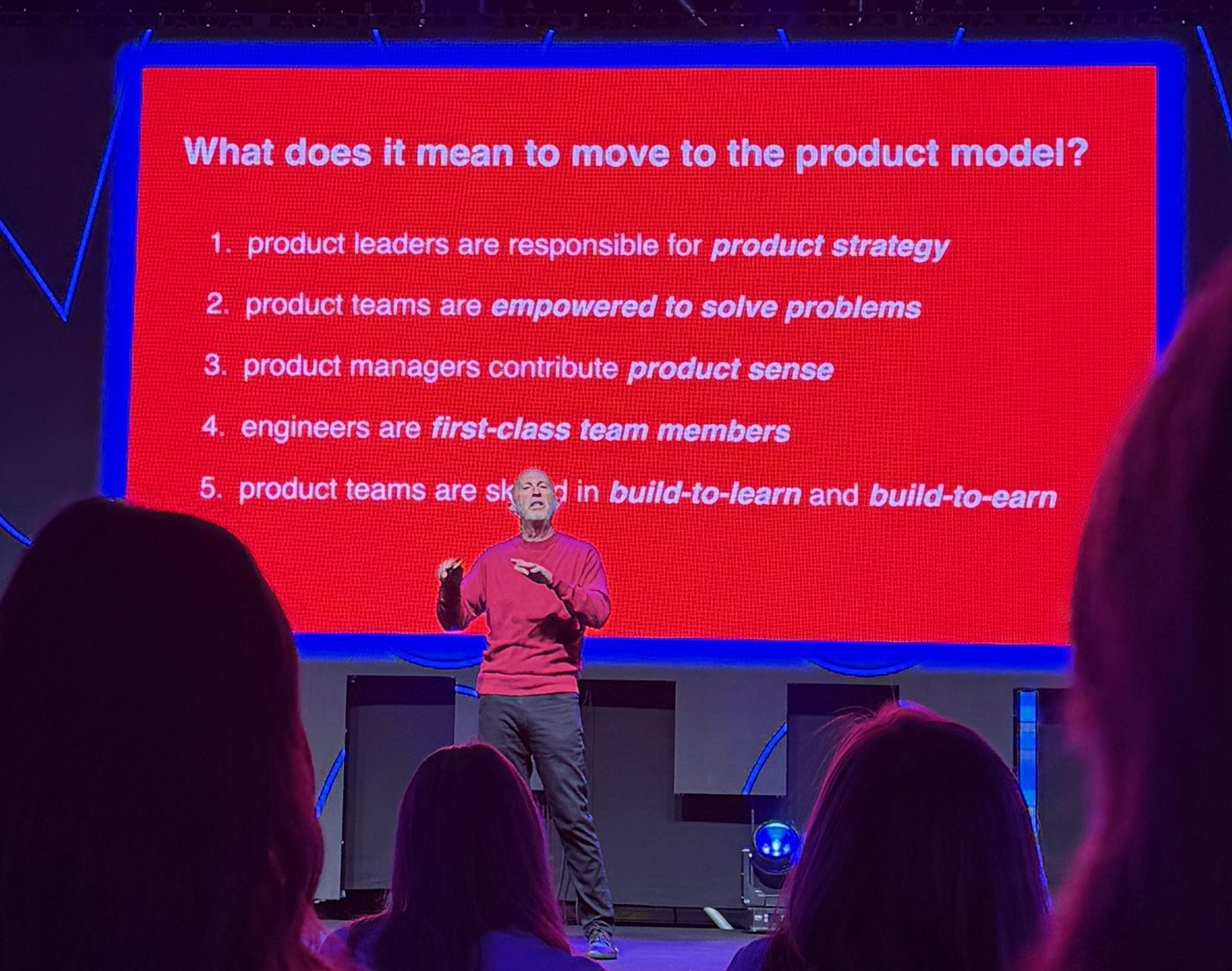 Marty Cagan in front of a slide: What does it mean to move to the product model? Product leaders are responsible for product strategy, product teams are empowered to solve problems, product managers contribute product sense, engineers are first-class team members, product teams are skilled in build-to-learn and build-to-earn.